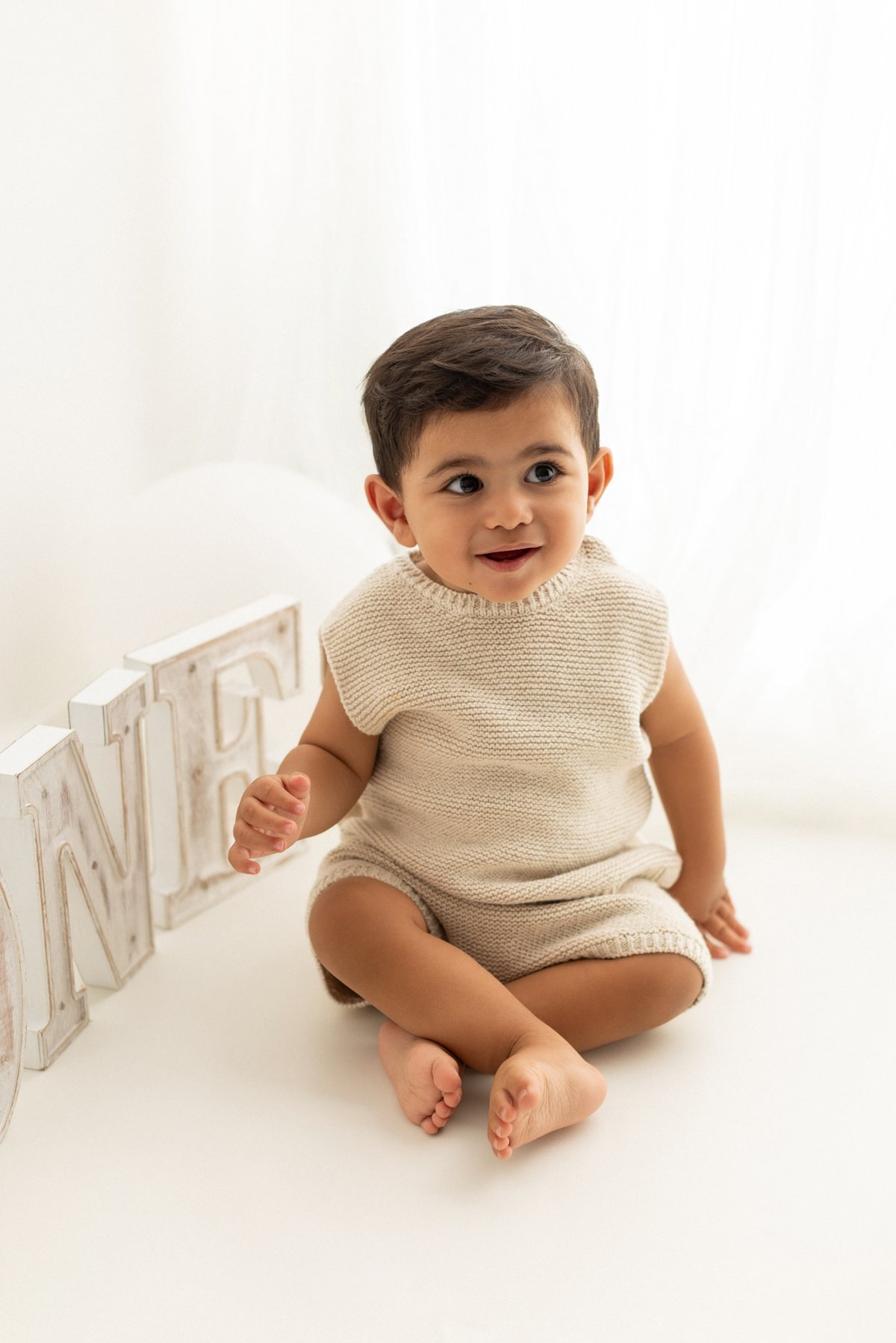 Baby sitting beside wooden ONE letters at a first birthday mini session