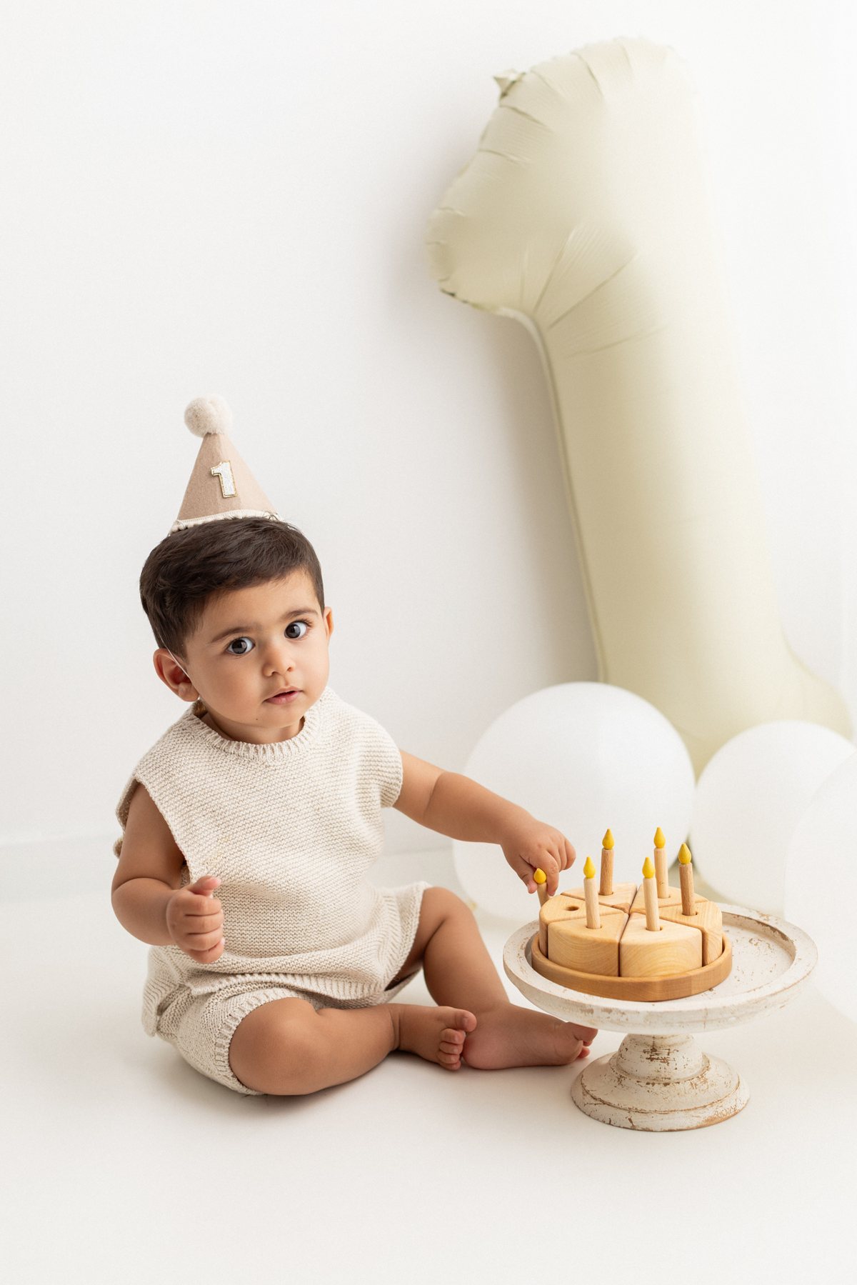 Baby in a party hat playing with a wooden toy birthday cake