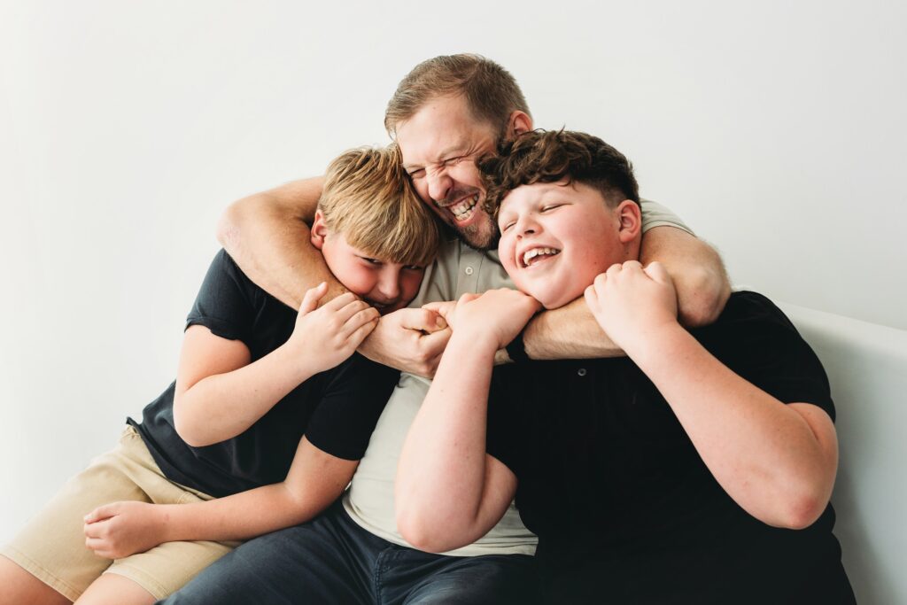 Dad and his two sons laughing in a big cuddle during a family photoshoot at the Barking studio
