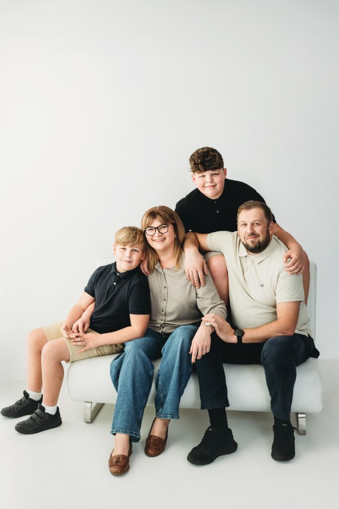 Family of four sitting close together on a white sofa, laughing, in a studio family portrait in Barking