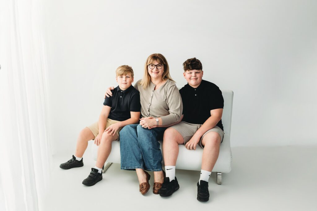 Mum sitting between her two sons on a white sofa in a family studio portrait
