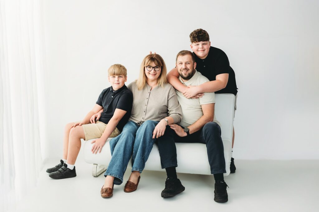 Mum, dad and two sons relaxed together on a white sofa against a pale studio wall